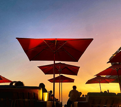 Red umbrellas at sunset on a rooftop with people relaxing.
