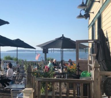 Outdoor cafe seating with umbrellas overlooking the ocean on a sunny day.