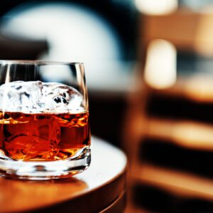 Glass of whiskey with ice on table.