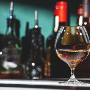 Glass of cognac with blurred bottles background.