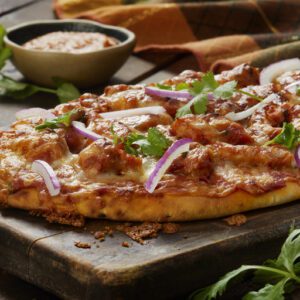 Delicious homemade pizza topped with cheese, herbs, and red onions on a wooden board.