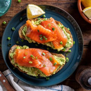 Avocado toast topped with smoked salmon and garnished with lemon and herbs.