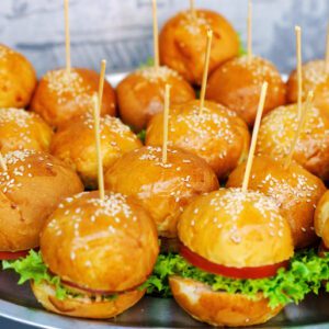 Mini chicken sliders on sesame buns with lettuce and sauce.