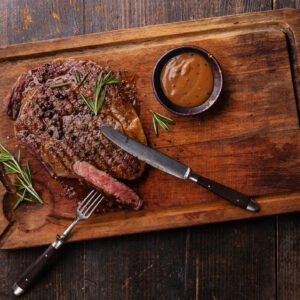 Sliced steak with sauce and rosemary on a wooden board.